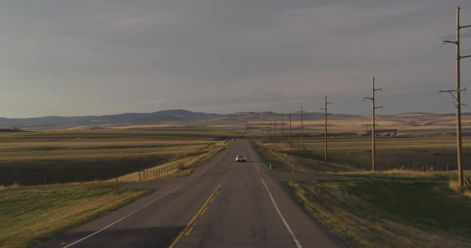 A sports car is traveling on country road surrounded by farmland and hills