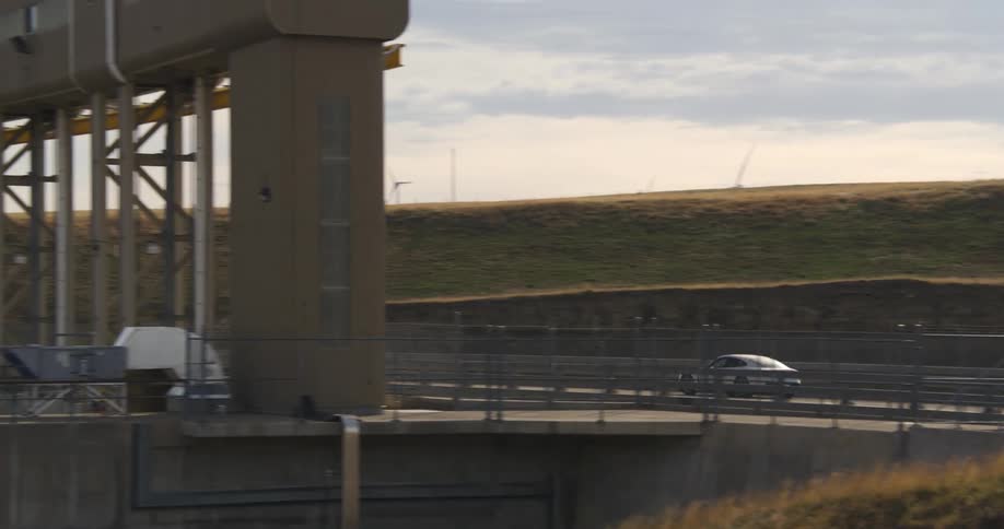 Car drives past wind farm and structure