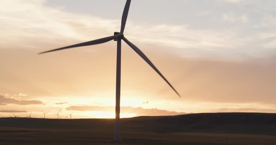 Wind turbine producing electricity is silhouetted against the sunset on wind farm