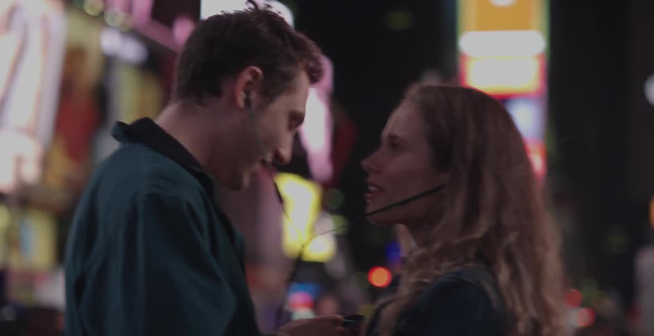 Couple sharing something through one pair of headphones in a large city at night