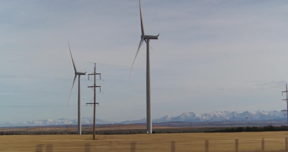 Traveling past two wind turbines in a dry field with mountains in the background