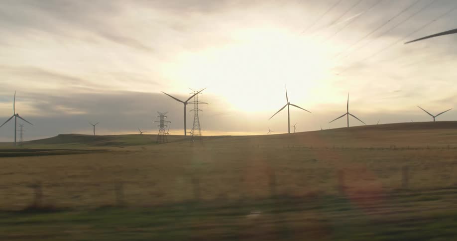 Passing by hilly farmland with an array of large windmills and power transmission towers in the daytime