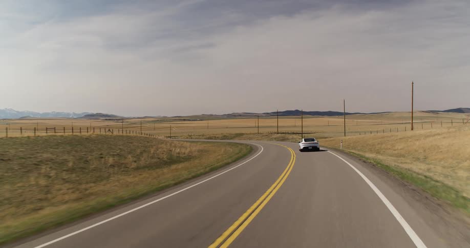 An electric car is driving down a road in a rural area