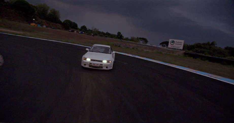 White race car drifting on a race track under storm clouds at evening