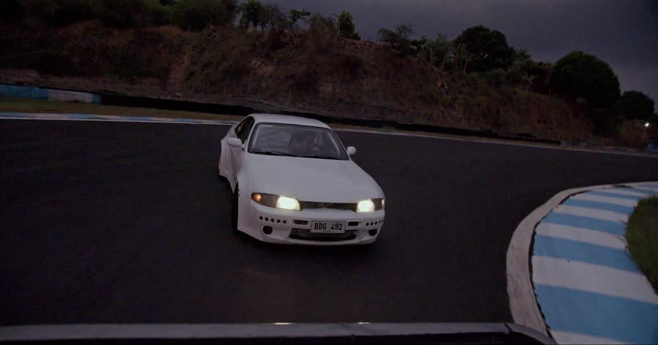 A race car drifts around a corner on a race track on a cloudy evening