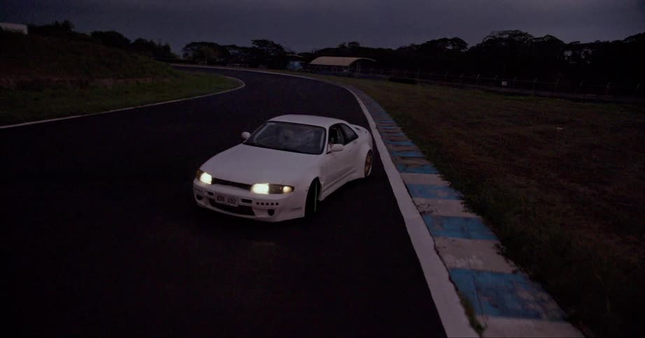 A white car with headlights on is sliding as it travels on a road
