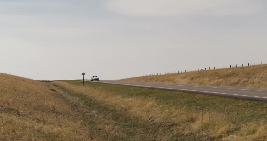 electric sports car driving on a road next to grassy fields with the sky and clouds in the background
