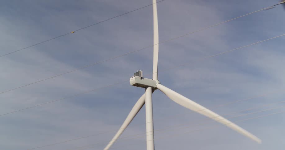Wind turbines spin near power lines under a cloudy sky