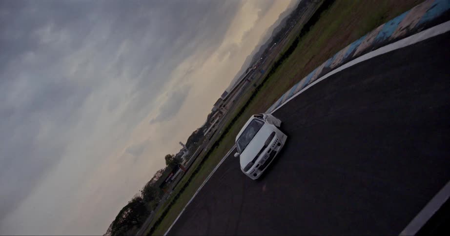 A white sports car races on an empty track drifting through a turn