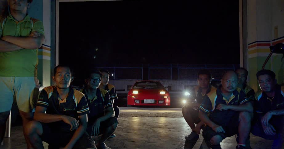 Garage mechanics pose with sports car in background at night