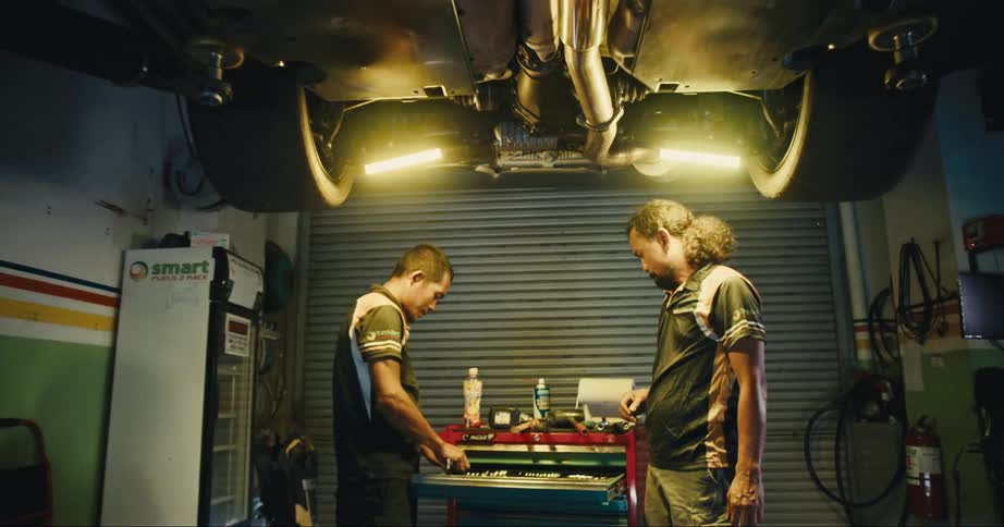 Car mechanics with blue shirts and shorts repair sport car at garage