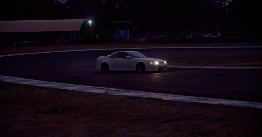 A white car with headlights on is sliding around a curve