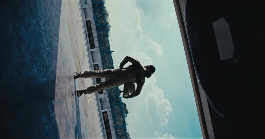 A race car driver stands in the entrance to a garage and looks out at the race track