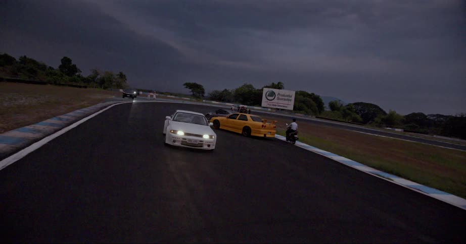A sports car drives past a motorcycle and another sports car on a race track