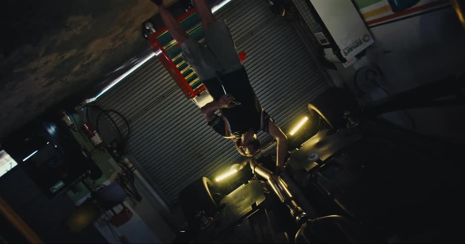 A man with a tool in a garage working on a vehicle with a wall and door in the background