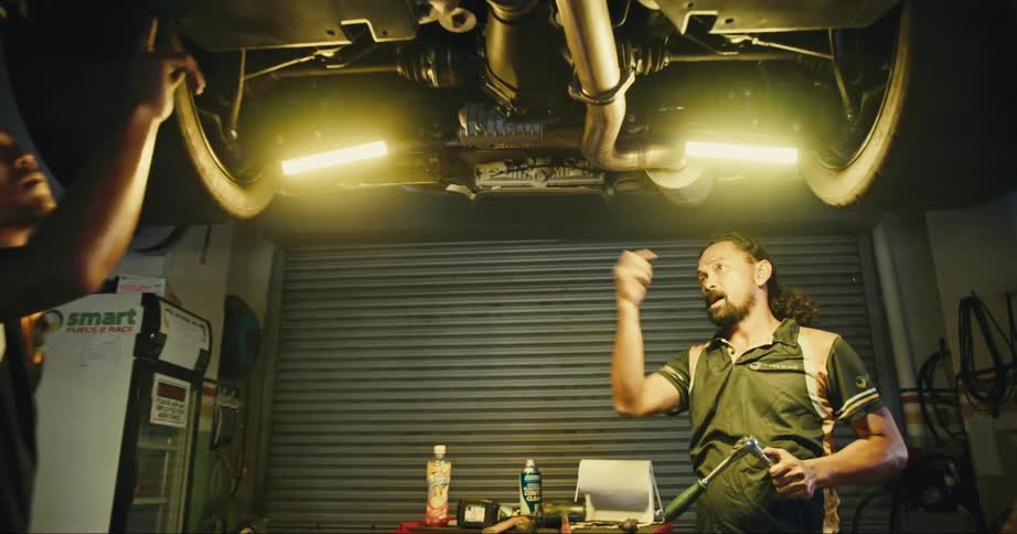 Two auto mechanics are in a garage working under a car that is up on a lift