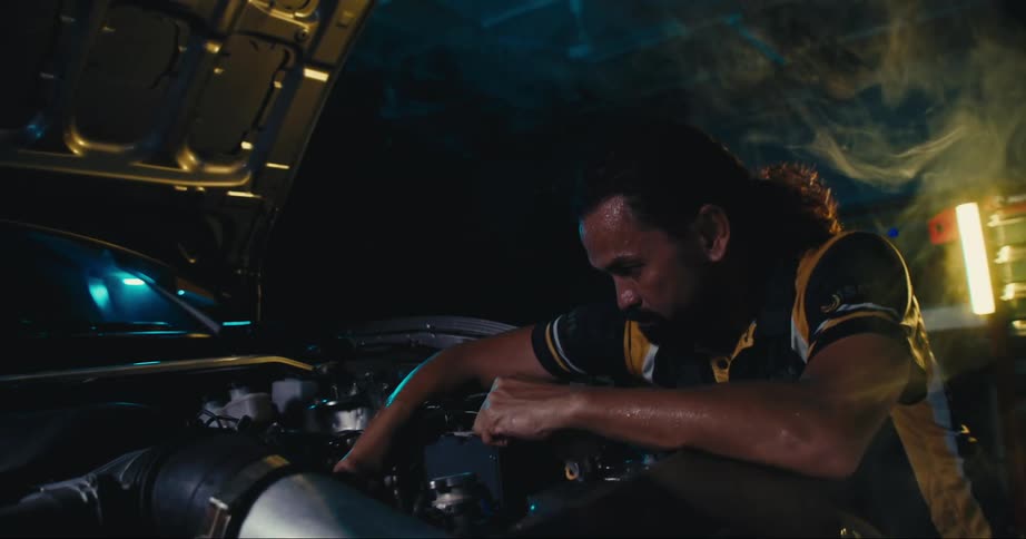 A man is working on a car engine in the dark garage