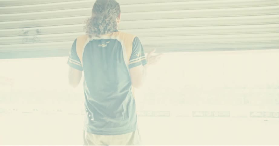Man with long hair black jersey shirt and shorts opens garage door in sunlight