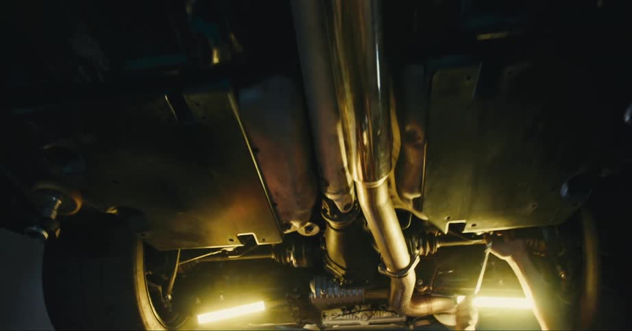 Two men in the garage working underneath a vehicle with a wall and door in the background