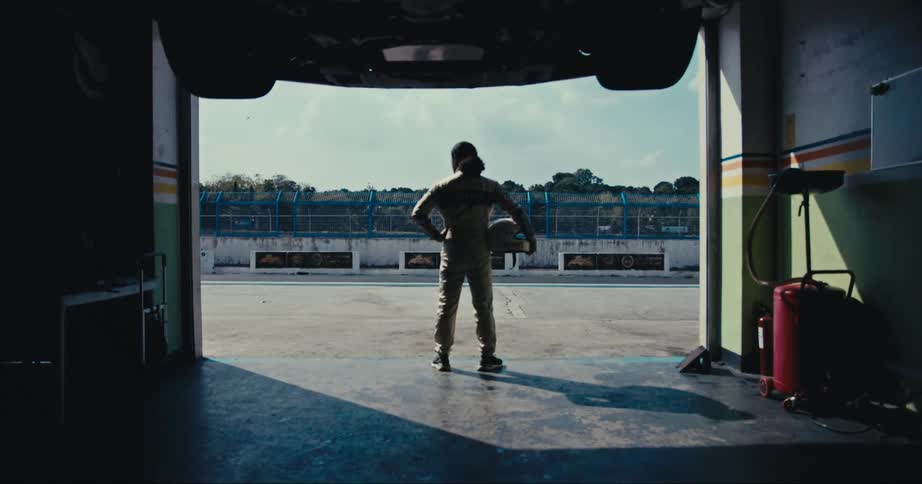 A race car driver is standing by the garage holding his crash helmet