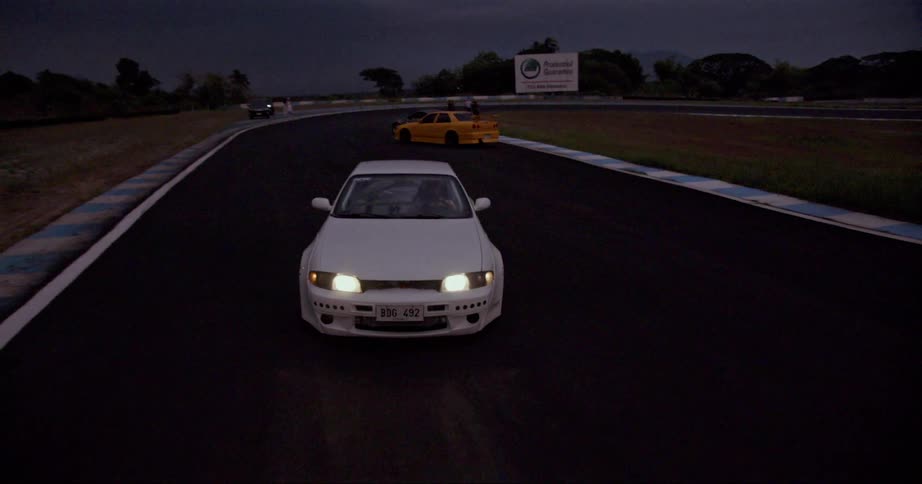 A car driving on a racetrack with trees the sky and clouds in the background