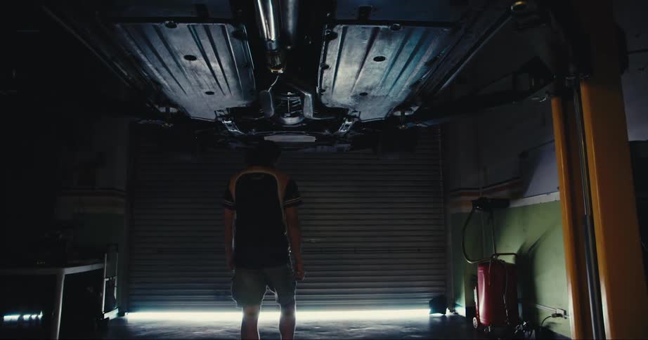 A male in shorts in a garage walking towards a garage door and sunlight
