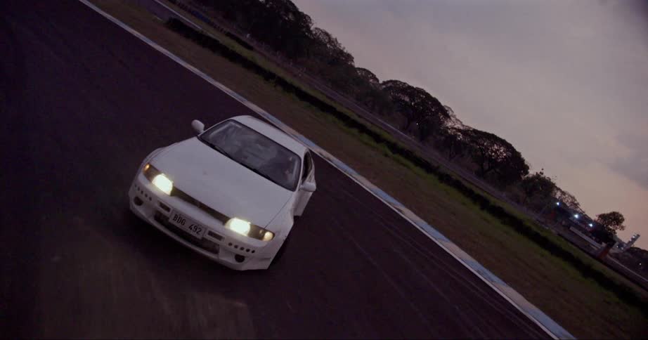 A white sportscar drifts around a curve on an empty track