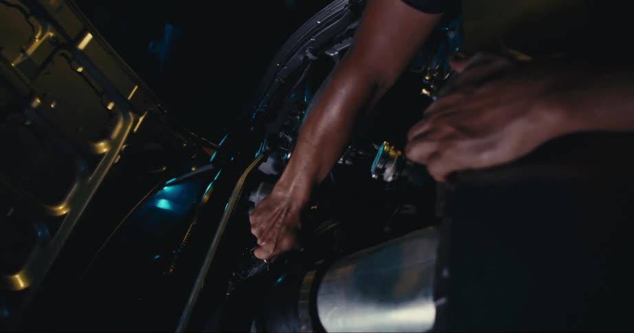 Man leans over working on car engine with hood fully opened