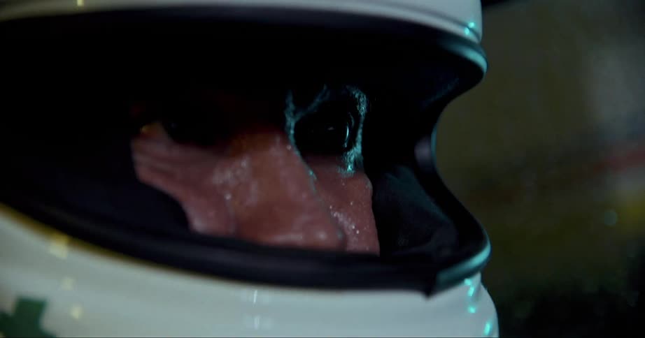 A race car drivers sweating face inside his helmet as he drives at night