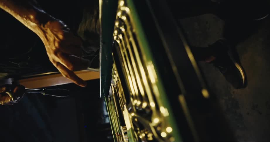 A man is in a dark lamp lit garage interacting with a tool drawer and tools during the day