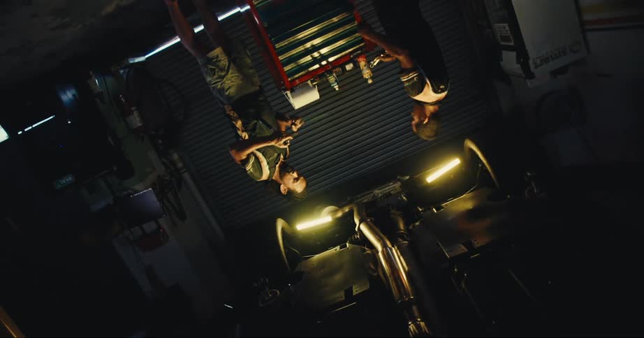 Two men are standing next to a tool chest in a large shadowy garage in the daytime
