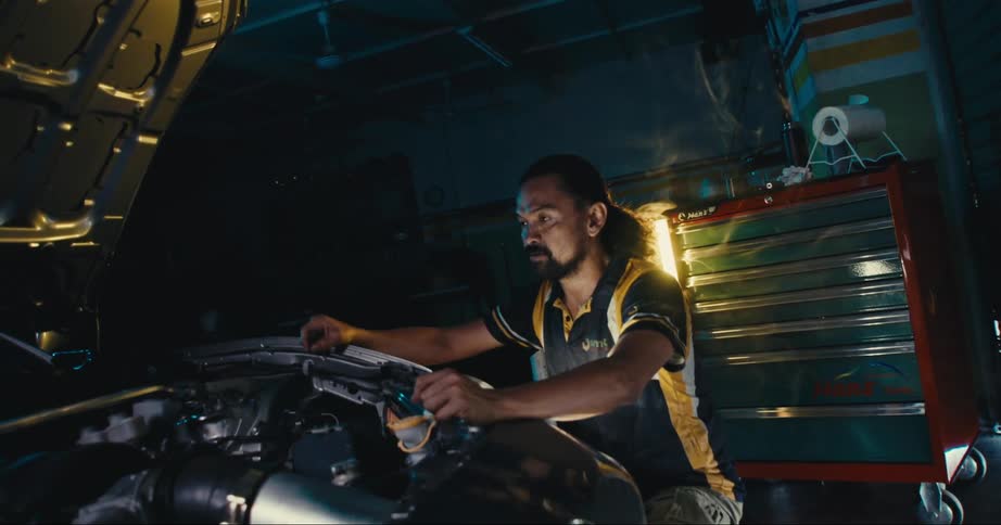 Mechanic working on the engine of a sports car inside a dimly lit shop