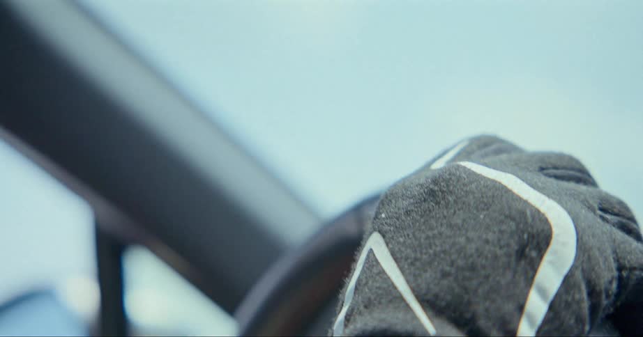Hand in a glove resting over a car steering wheel