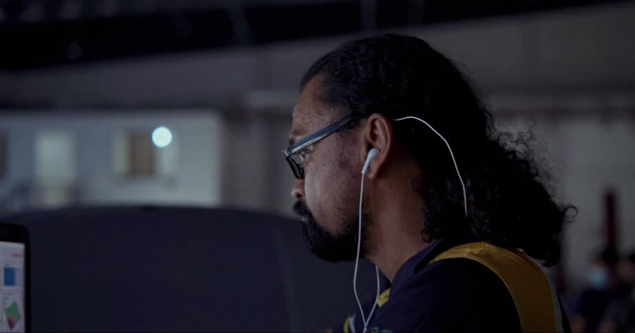 A man with glasses in a garage using a laptop on top of a vehicle