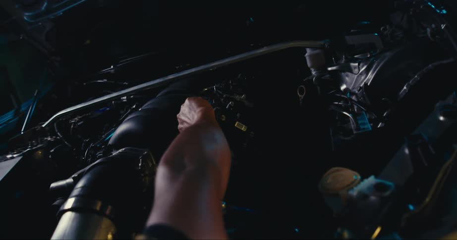 Man in a colorful tshirt fixing the engine of a sports car at night
