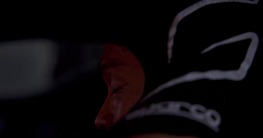 Lights reflect on a mans face as he puts on a racing helmet