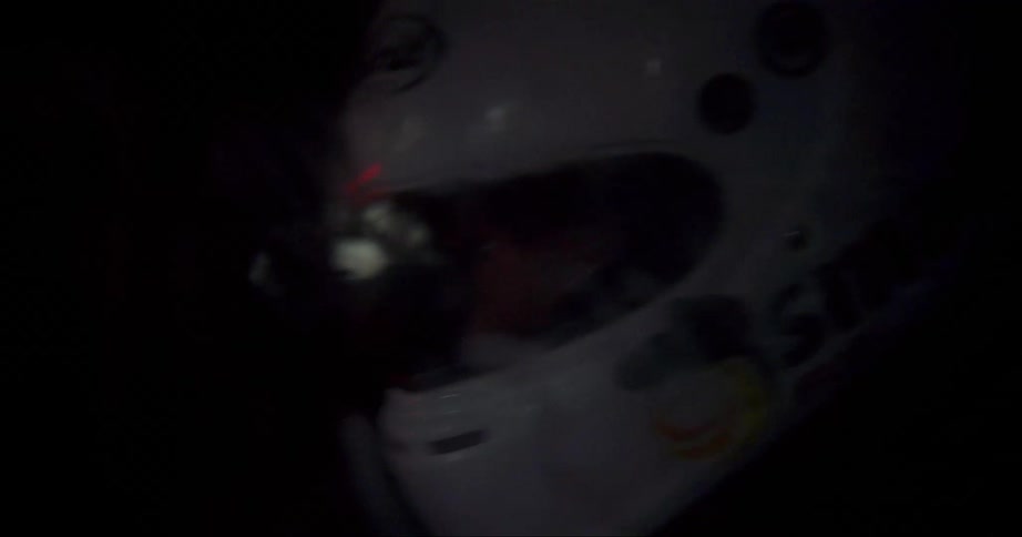 The helmeted head of a race car driver as he races at night