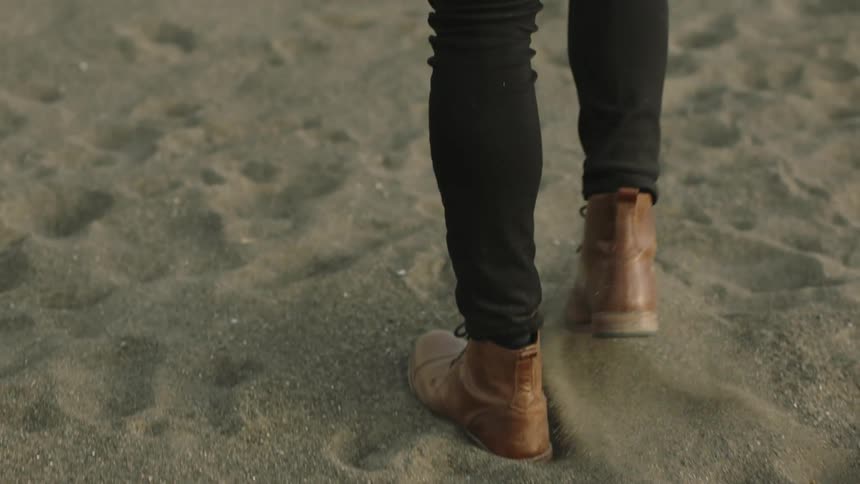 Person wearing laced ankle boots walks across sand before stopping