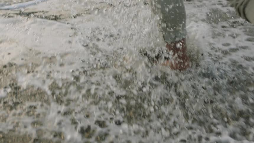 A man reaches down to run his hand through sand and water while running toward the ocean