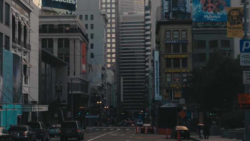 A city street with vehicles and people with buildings the sky and clouds in the background