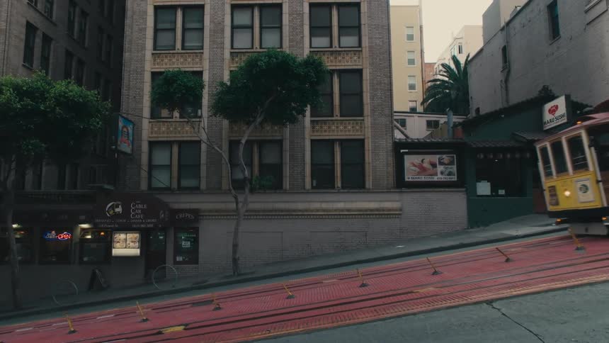 A street car travels down a sloped road in a city during the day