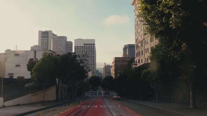 A city street with vehicles and trees with buildings the sky and clouds in the background