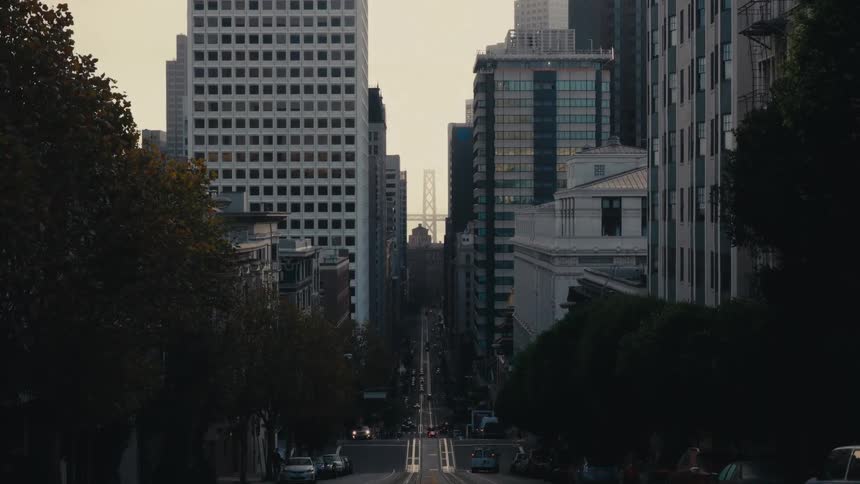 A city street with vehicles and trees with buildings the sky and clouds in the background