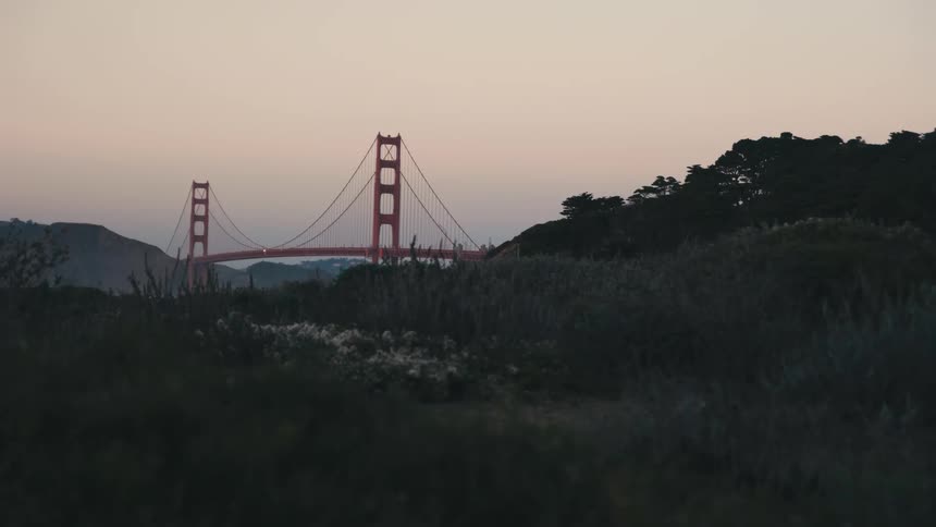 The golden gate bridge seen from a distance among trees and mountains