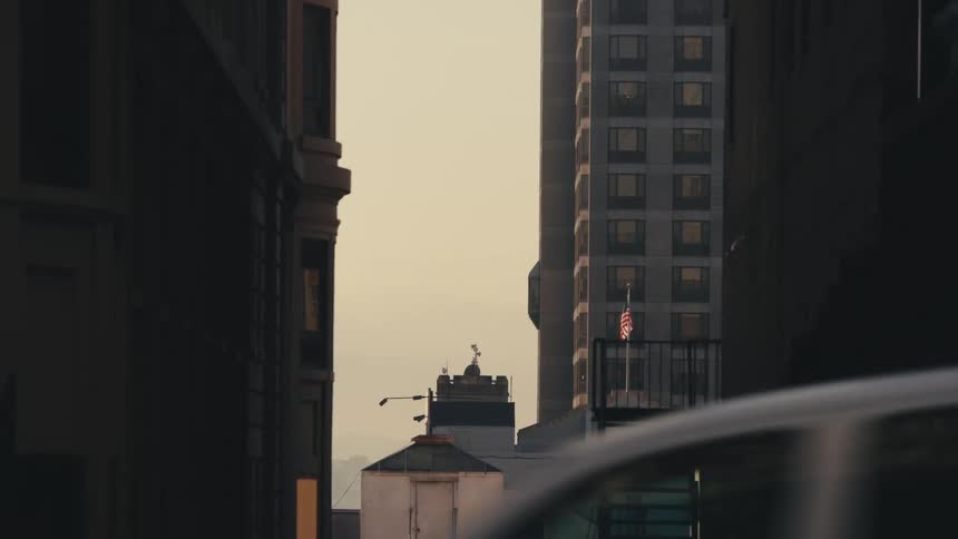 A city with vehicles an american flag and buildings with the sky and clouds in the background
