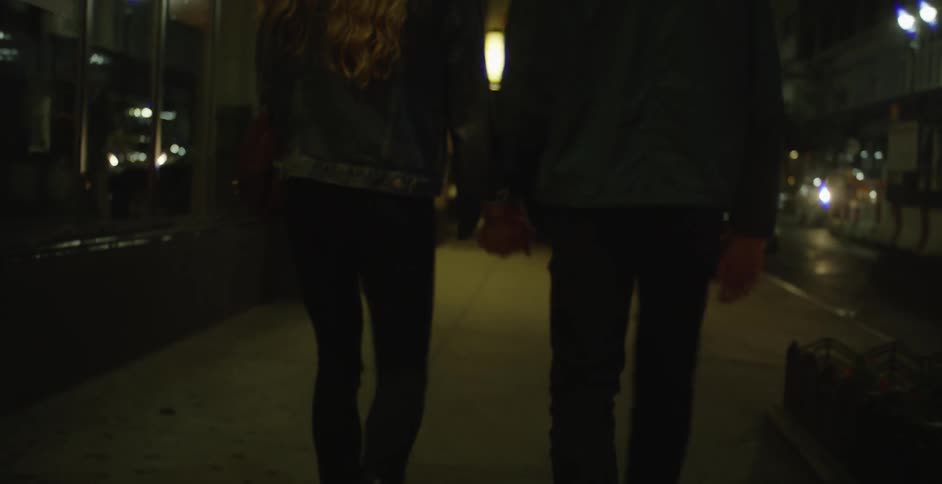 Couple walking down a city street while holding hands at night