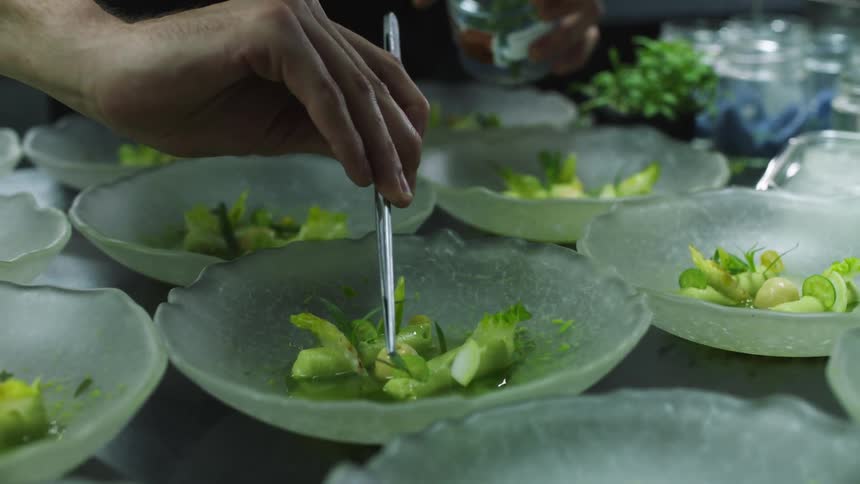 A person is placing food in rows of dishes on the table