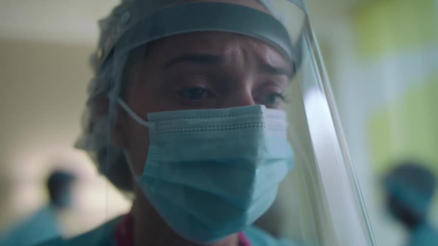 A nurse with a mask scrubs and a face shield in a hospital room