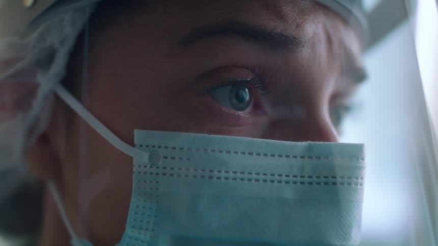 Medical professional wearing medical mask and face shield stars out window before walking away