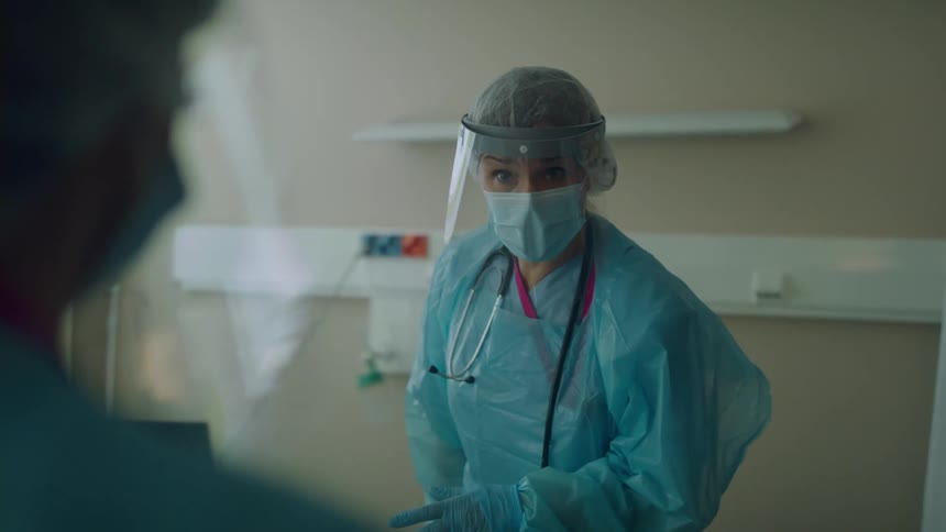 Doctors in scrubs and masks are chatting in a hospital room